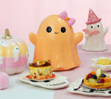 Fantôme Halloween souriant orange pastel à nœud rose, posé sur une table de goûter d'Halloween