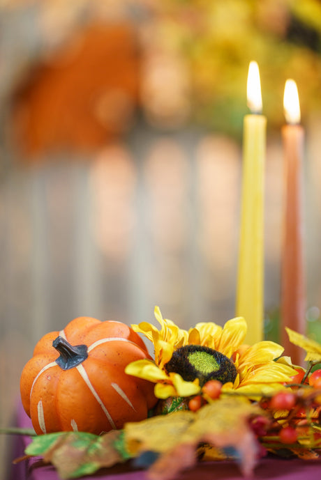 Détail d'une décoration de table d'automne : tournesol, citrouille orange, feuilles et bougies